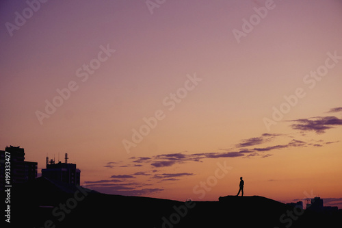 Silhouette people standing on hill at sunset time over city. 