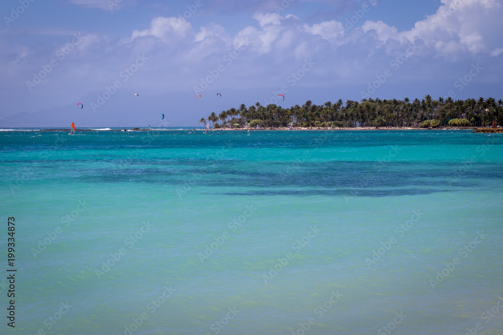 Turquoise and crystal clear sea in Guadeloupe, Sainte-Anne bay and beach. Windsurfers and kitesurfers enjoying the sport in background