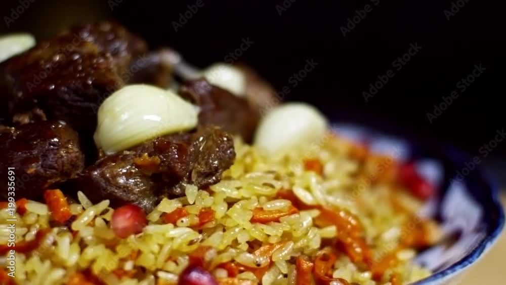 Close up shot of rice pilaf with meat and carrots and cloves of garlic on top, cook sprinkling dish with pomegranate seeds Close up shot of rice pilaf with meat and carrots and cloves of garlic on top, cook sprinkling dish with pomegranate seeds