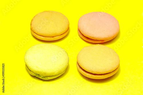 Delicious four multicolored macaroon on a yellow background