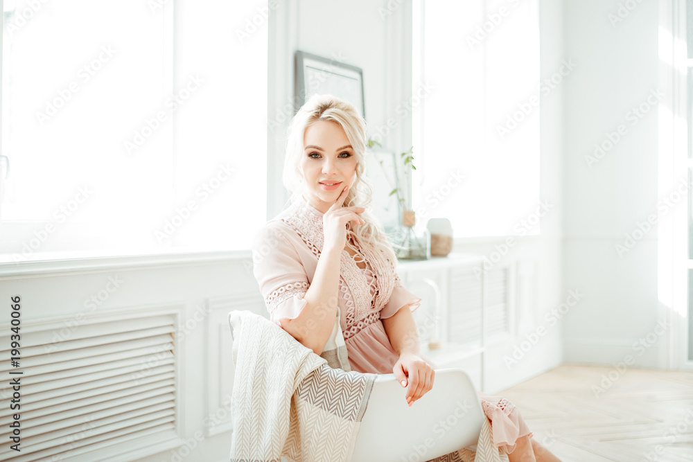 comfort of home and interior. Portrait of a young blonde in a pink dress on a beautifully decorated living room background in soft pastel colors. A woman in a rocking chair resting at home comfort of home and interior. Portrait of a young blonde in a pink dress on a beautifully decorated living room background in soft pastel colors. A woman in a rocking chair resting at home