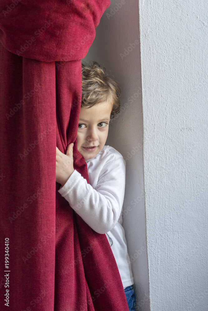 Child hiding behind a red curtain with smiling gesture Child hiding behind a red curtain with smiling gesture