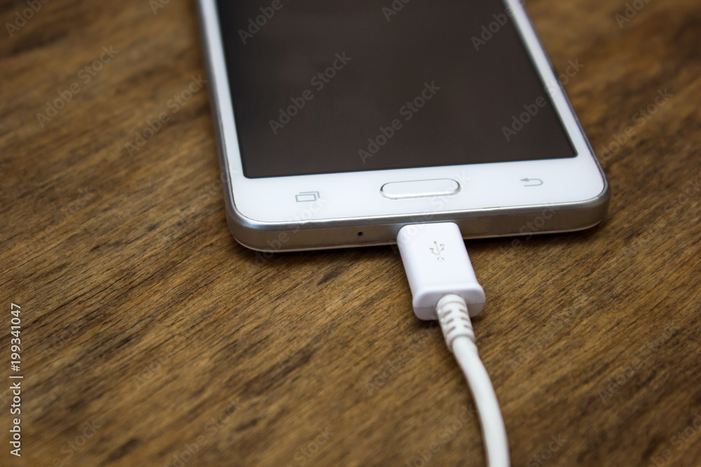 Charging a smartphone using a power supply on a wooden board Charging a smartphone using a power supply on a wooden board