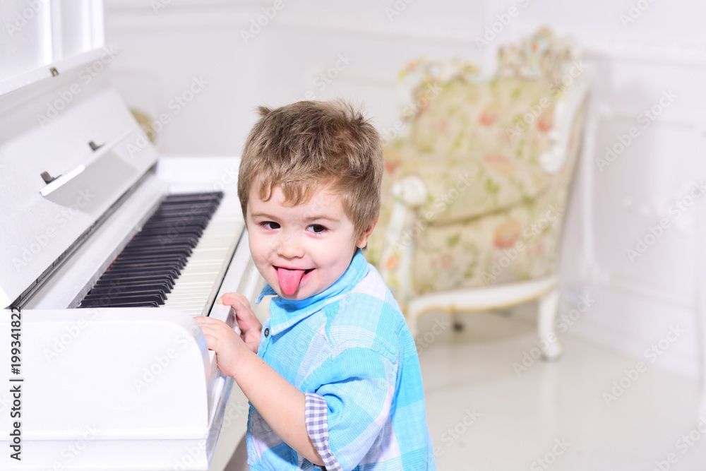 Child sit near piano keyboard, white background. Boy cute and adorable puts finger on keyboard of piano. Elite childhood concept. Kid spend leisure near musical instrument. Child sit near piano keyboard, white background. Boy cute and adorable puts finger on keyboard of piano. Elite childhood concept. Kid spend leisure near musical instrument.