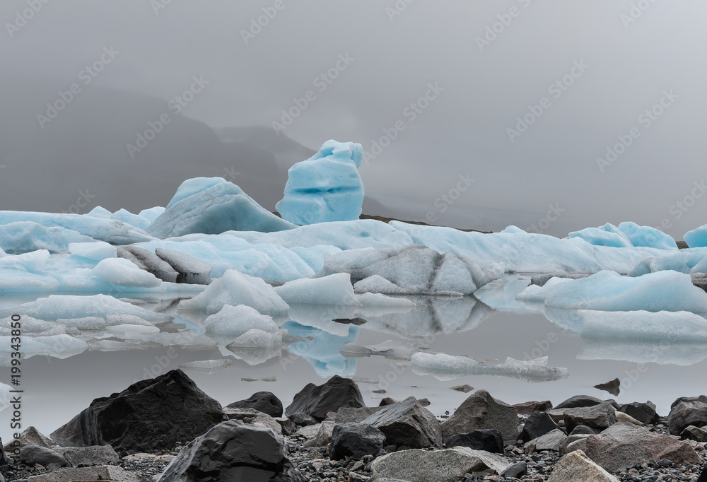 blaues Eis auf Wasser mit Steinen im Vordergrund