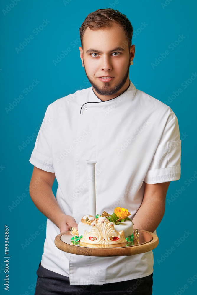 young male confectioner in a tunic with cake in the studio young male confectioner in a tunic with cake in the studio