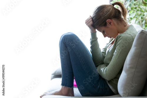 Unhappy lonely depressed young woman sitting on sofa at home. Depression concept.