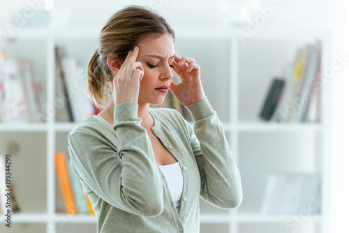 Unhealthy young woman with headache touching his head at home.