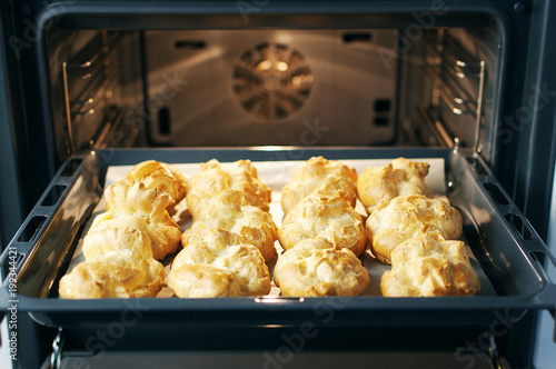 Homemade profiteroles in the oven. Process of baking cookies, French dessert, confectionery background.  photo