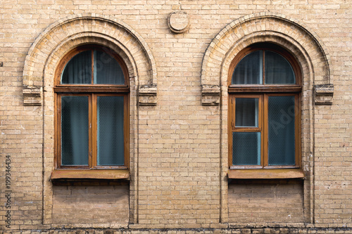 Two vintage arched windows in a wall of yellow bricks. Green - the colors of sea wave glass in a maroon dark red wooden frame. The concept of antique vintage architecture in building elements