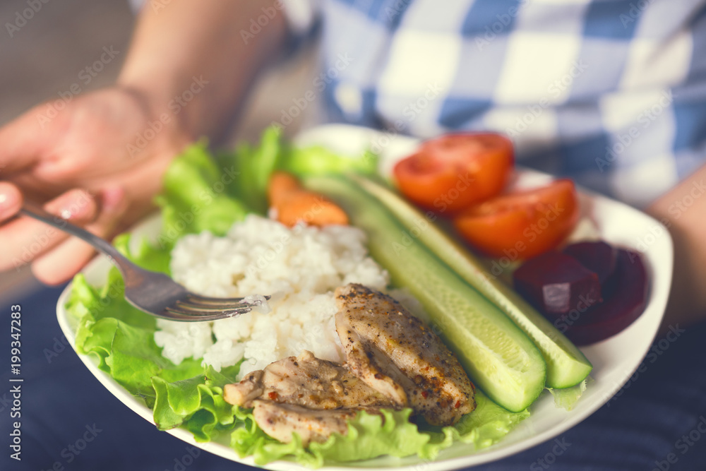 A girl holds a plate with vegetables and chicken meat with spices. Healthy eating concept. Girl in jeans and a plaid shirt. Proper nutrition. Diet. Health. Chicken meat with spices. Small depth of A girl holds a plate with vegetables and chicken meat with spices. Healthy eating concept. Girl in jeans and a plaid shirt. Proper nutrition. Diet. Health. Chicken meat with spices. Small depth of