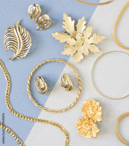 Woman's Jewelry. Vintage jewelry background. Beautiful gold tone brooches, braceletes, necklaces and earrings on blue background. Flat lay, top view.