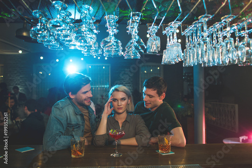 They are so boring. Disappointed female with pain in head hearing communication of two cheerful men. Rest in club concept