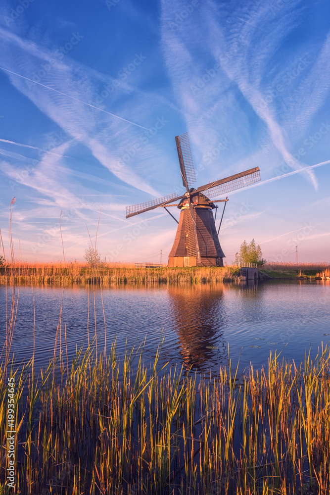 Scenic sunset landscape with windmill, blue sky and reflection in the water. Traditional dutch countryside, famous village of mills Kinderdijk, Netherlands (Holland), vertical image