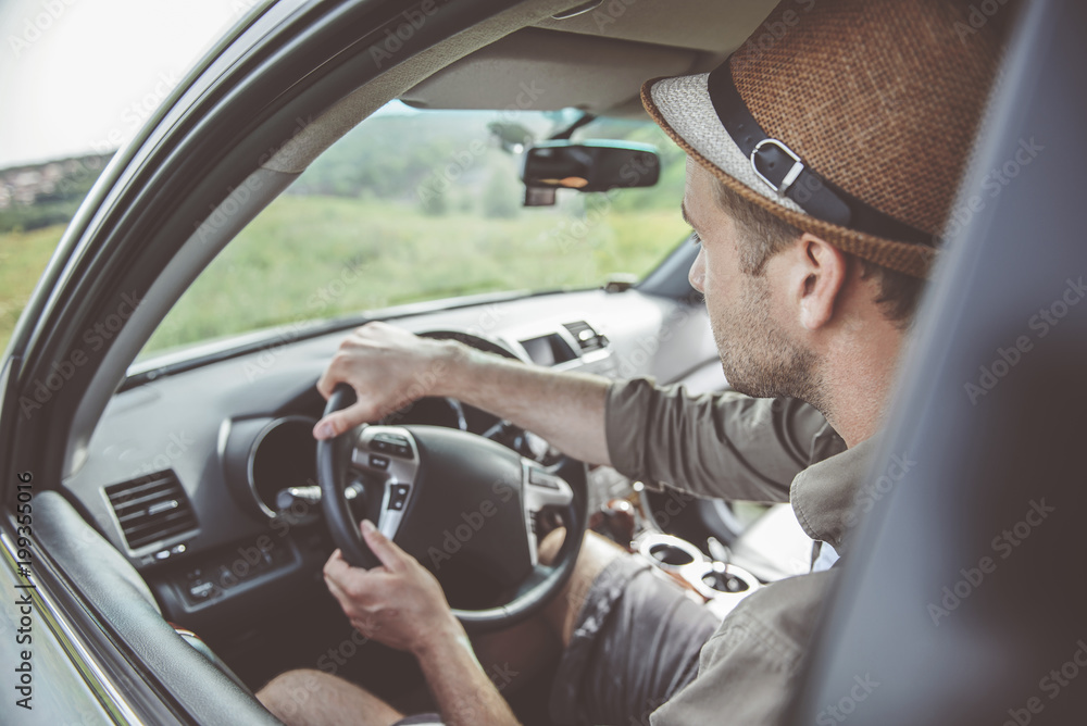 Side view of serious young man is driving his car with concentration. He is traveling across country. Selective focus Side view of serious young man is driving his car with concentration. He is traveling across country. Selective focus