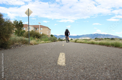 фотографія Solo man bicycling down empty road towards the mountains in New Mexico