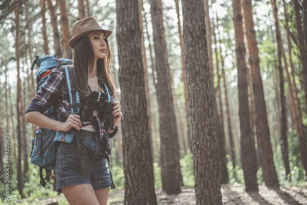 Travel adventure. Concentrated backpacking girl tourist is walking in forest. Copy space in the right side