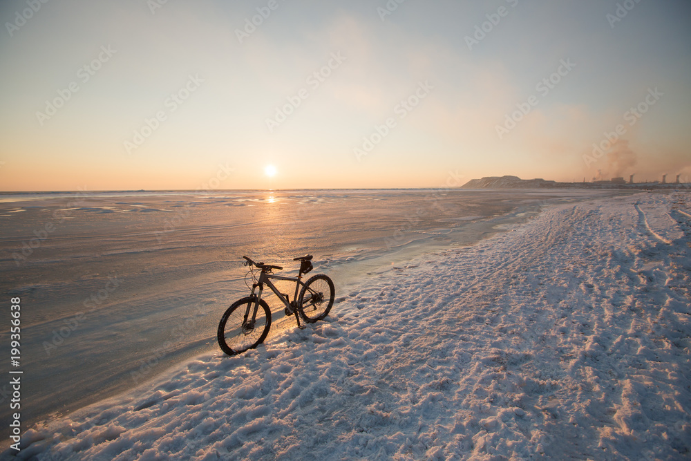 Fototapeta premium Mountain bike stay in snow near frozen sea or lake. Winter bicycle exploitation and maintenance. Studded tires