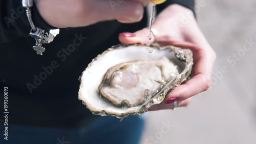 Close-up shot of women pouring lemon juice on the open oysters at the street. Delicious seafood in hand, Dynamic Slow motion
