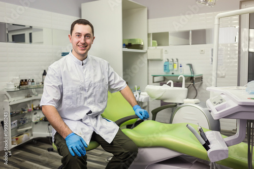 Male dentist standing over medical office background. Healthcare  profession  stomatology and medicine concept