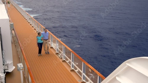 Retired senior couple walk on deck of cruise ship and look at ocean