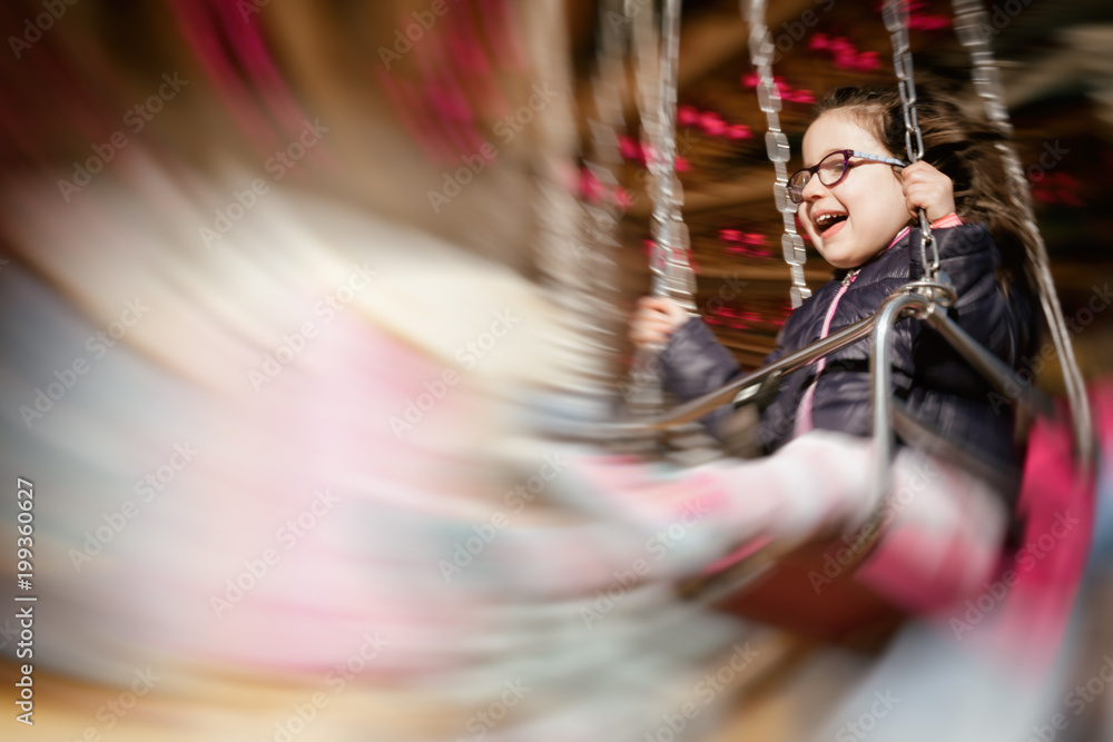 Panning shot of a little girl smiling while riding a carrousel; intentional motion blur effect.
