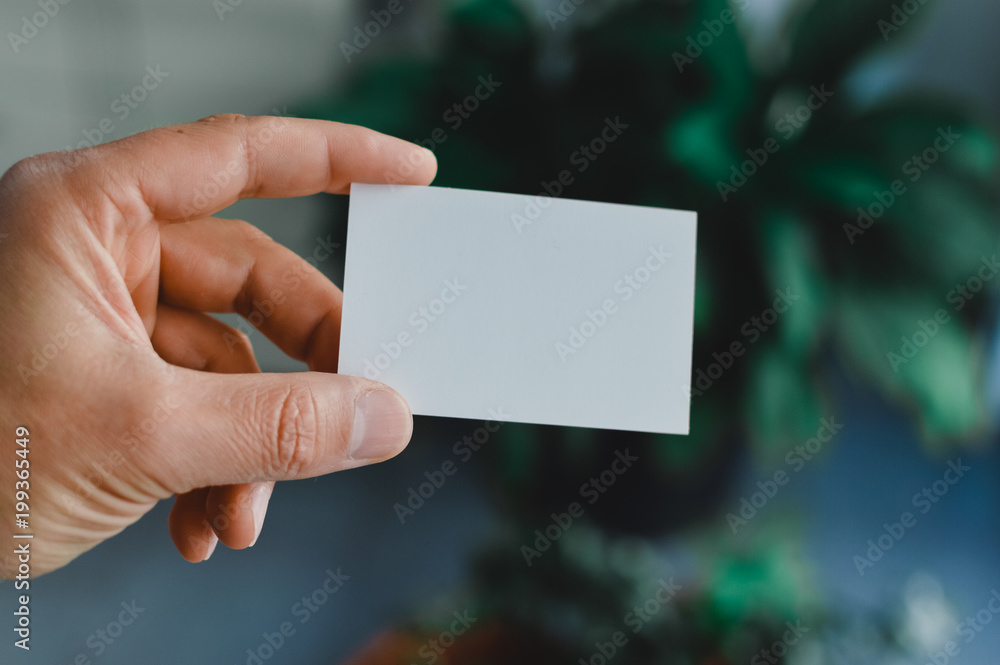 Close up on hand of a businessman showing business card office space background Close up on hand of a businessman showing business card office space background