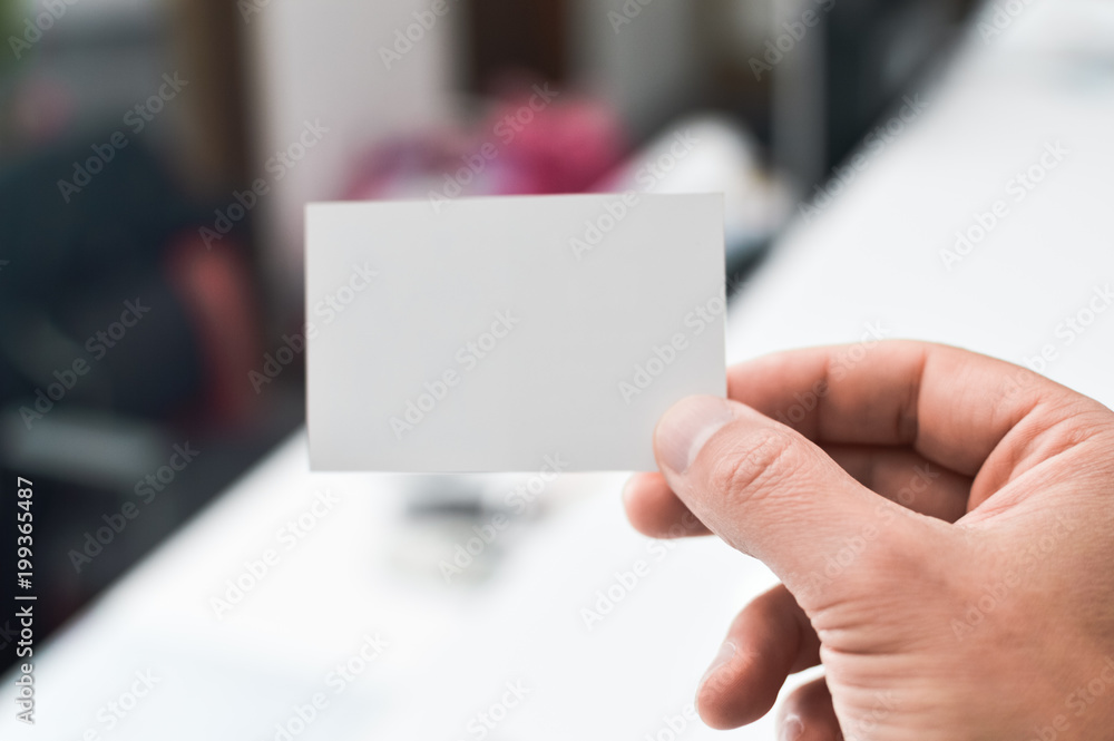Close up on hand of a businessman showing business card office space background Close up on hand of a businessman showing business card office space background