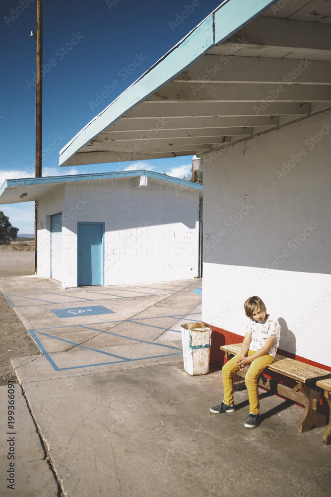 Full length of boy sitting on bench against house during sunny day Full length of boy sitting on bench against house during sunny day
