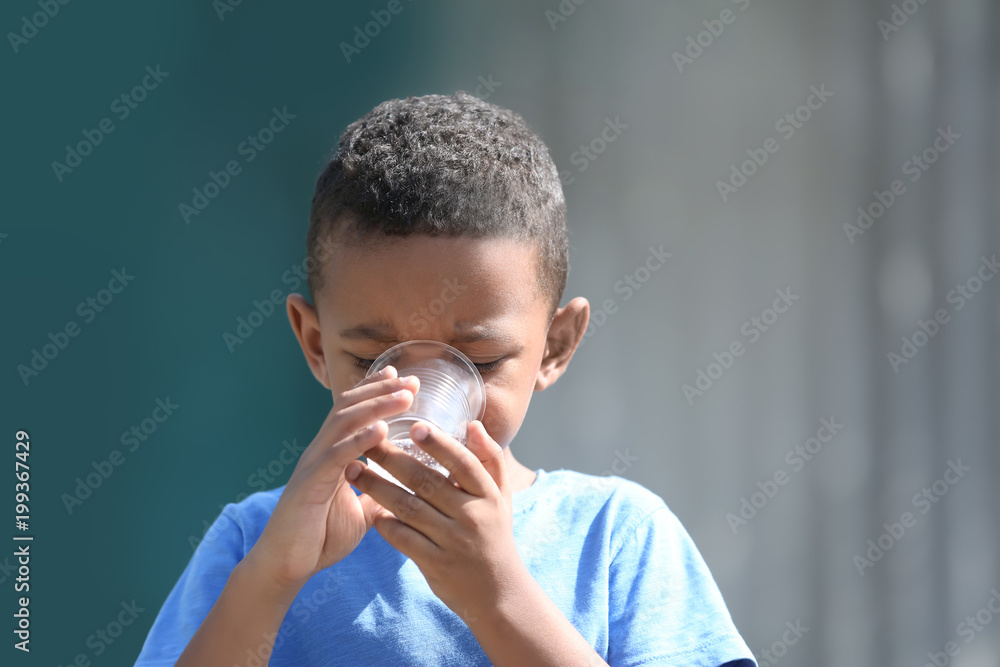 Cute African American boy drinking water from plastic cup, outdoors Cute African American boy drinking water from plastic cup, outdoors