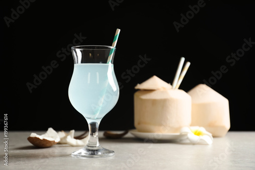 Glass with fresh coconut water on table against black background