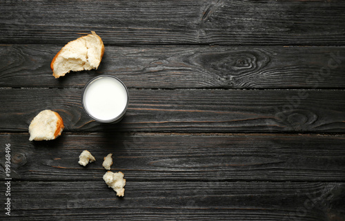 Glass of milk and bun pieces on wooden background, top view