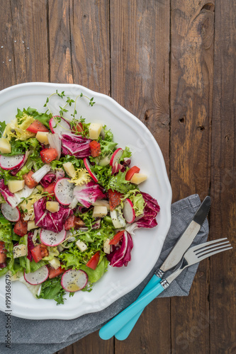 Fresh salad with mixed greens, radish, cheese and tomato in a plate on wooden background. Italian Mediterranean or Greek cuisine.