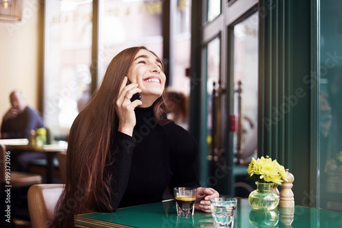 Young woman with long hair laugh and smile, drinking coffee having rest in cafe near window