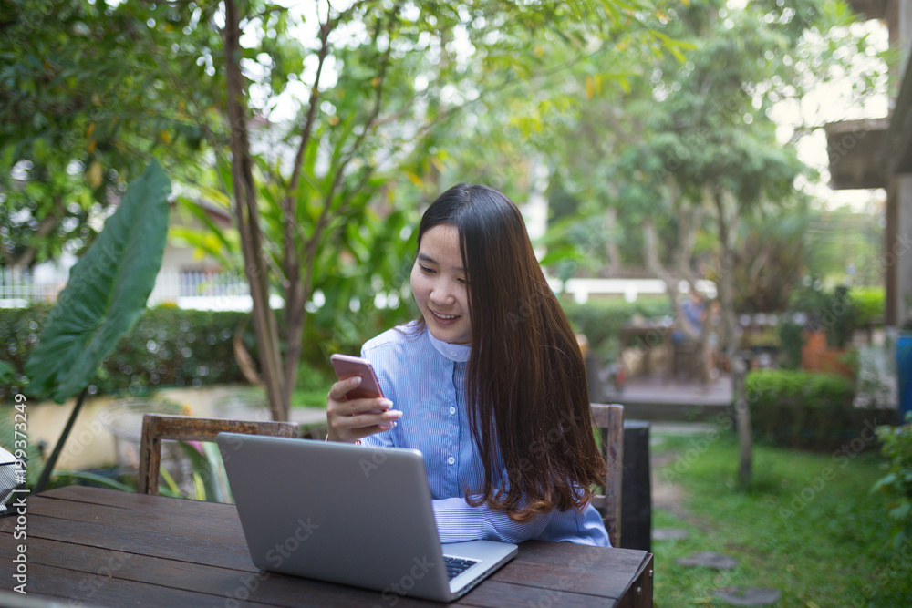 Women sitting and using smartphone and laptop on the table and she is feeling happiness at garden or cafe shop. Women sitting and using smartphone and laptop on the table and she is feeling happiness at garden or cafe shop.