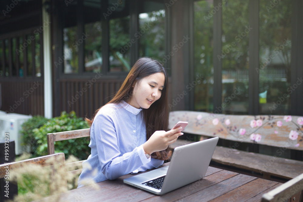 Women sitting and using smartphone and laptop on the table and she is feeling happiness at garden or cafe shop. Women sitting and using smartphone and laptop on the table and she is feeling happiness at garden or cafe shop.