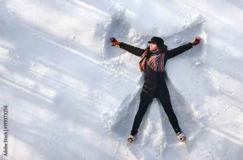 A girl on the snow shows an angel. Spreading arms. Top view. Drone. Smile. Happy.
