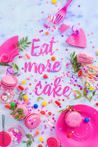 Party concept with Eat more cake paper text, candies, sweets, confetti and macarons. Colorful Birthday celebration flat lay.