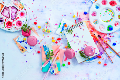 Sweettooth artist tools creative party concept. Pink macarons in a colorful party activity concept with confetti, artist tools, brushes, palette and sketchbook with blank pages.
