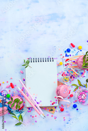 Open notepad with blank pages in an organizing a party concept with confetti, pink macarons, candies and sprinkles. Creative Event To-do list flat lay with copy space.