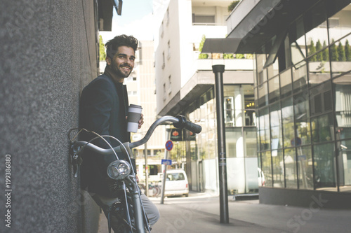 Smiling businessman on street with bike standing and holding cup of coffee. Space for copy.
