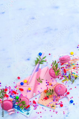 Party invitation concept. Love letter in a pink envelop with macarons, candies and confetti on a light background with copy space.