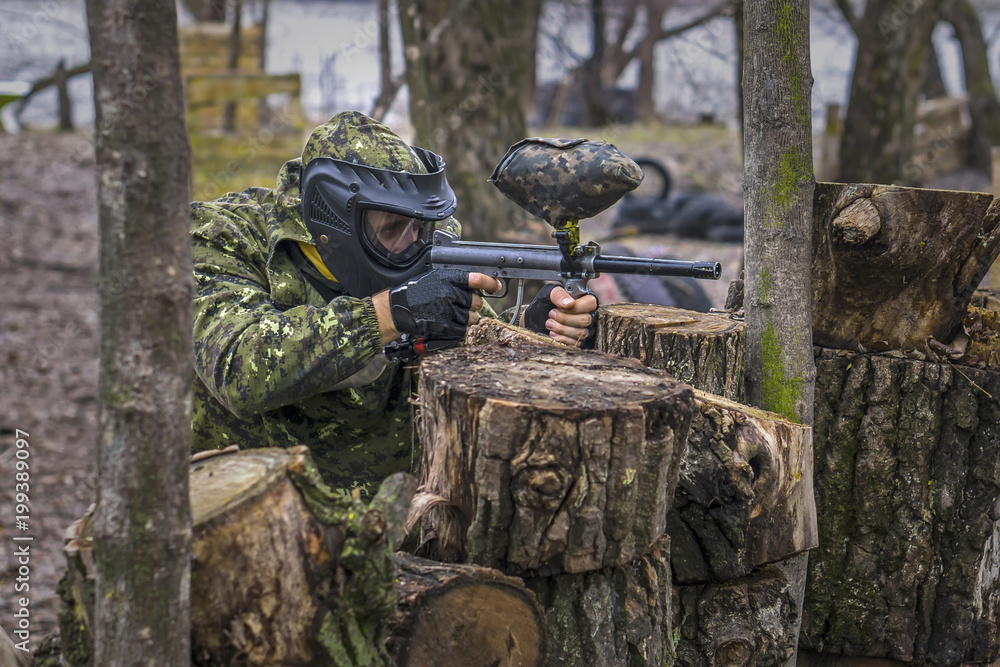 Paintball player takes aim, hides and shooting. Man wearing protective equipment Paintball player takes aim, hides and shooting. Man wearing protective equipment