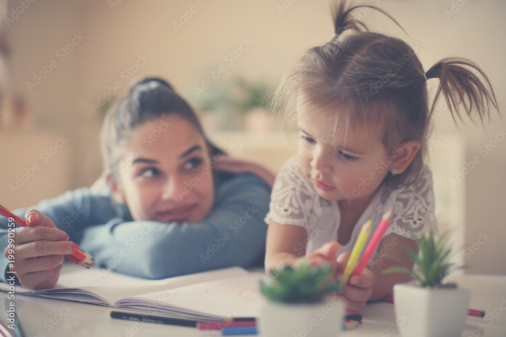 Mother and daughter enjoying together at home and coloring book. Close up.