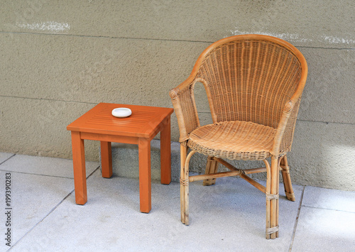 Rattan chairs with mini wooden table against rug cement wall.