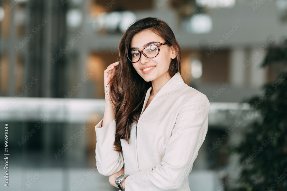 Fototapeta premium Beautiful Russian business girl with glasses, standing with arms crossed and smiling. Office style and business image, business meeting and greeting