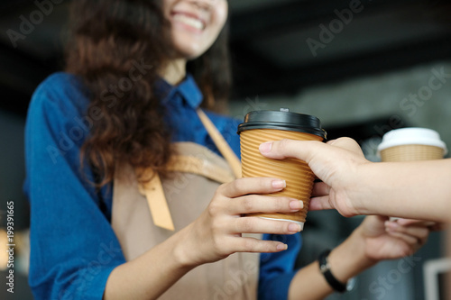 Young asian woman barista serving a disposable coffee cup to customer at cafe counter background, small business owner, food and drink industry concept