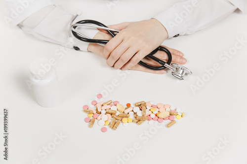 Doctor at white desk with handful pills in office in hospital. Woman holds in hands stethoscope in consulting room. Medicine concept. Copy space advertisement. With place for text. Advertising area.