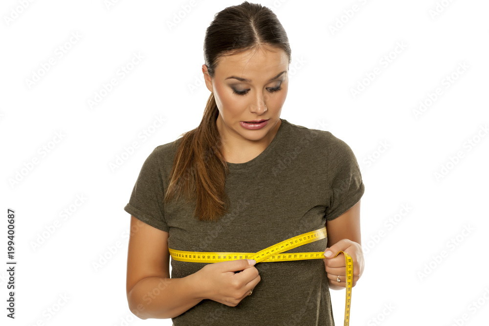 Worried young woman measuring her breasts on white background Worried young woman measuring her breasts on white background