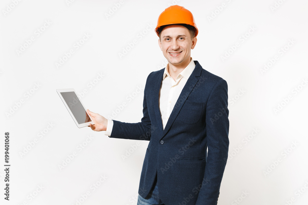 Young handsome smiling businessman in dark suit, protective hardhat holding tablet pc computer with blank screen isolated on white background. Male worker for advertisement. Business, working concept. Young handsome smiling businessman in dark suit, protective hardhat holding tablet pc computer with blank screen isolated on white background. Male worker for advertisement. Business, working concept.